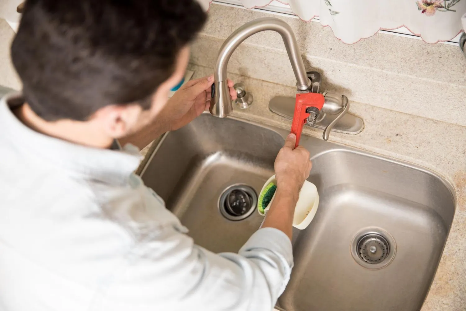 Plumber tightening a kitchen water faucet with a wrench