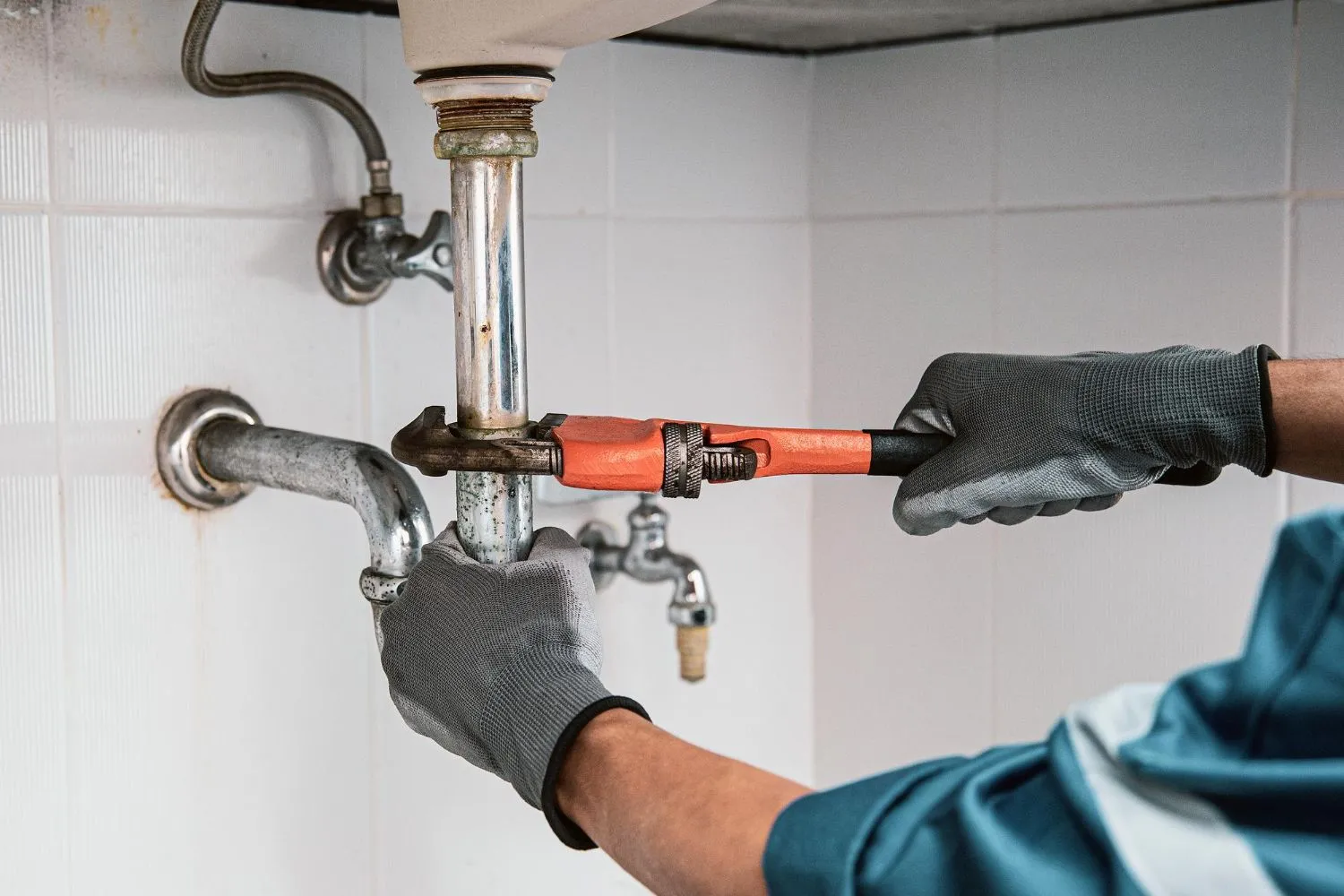 Plumber using a wrench to repair a water pipe under a sink